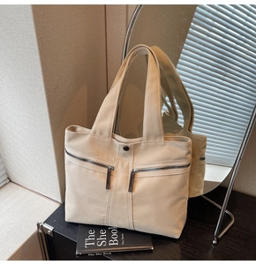 Detail of beige canvas tote bag showing outer zipper pockets and dark brown leather accents