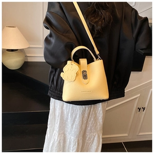 Detail of light yellow lychee pattern leather bucket bag with cute dog charm and silver lock