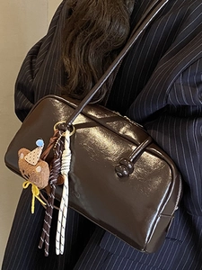 Brown glossy leather bowling bag with cute bear charm worn over a dark blazer