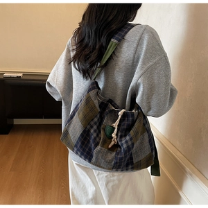 Rear view of a model wearing a large plaid tote bag with wide strap and drawstring detail