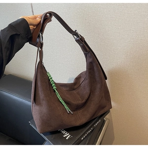 Close-up of brown suede hobo bag featuring a green braided rope charm and silver hardware
