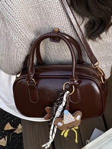 Sac Boston moderne en cuir marron foncé avec poignées et breloque ours à la lumière du soleil