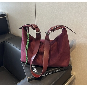 Detail of burgundy suede hobo bag with adjustable strap and green woven keychain charm
