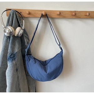 Detail view of a blue nylon crescent bag hanging on a rack with lifestyle accessories