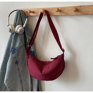 Macro detail of a burgundy nylon crescent bag hanging on a wooden hook with lifestyle props
