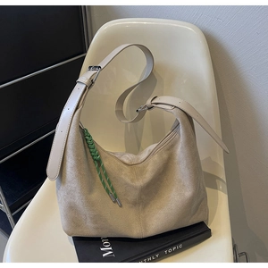 Detail of beige suede hobo bag with woven rope accent on a minimalist chair