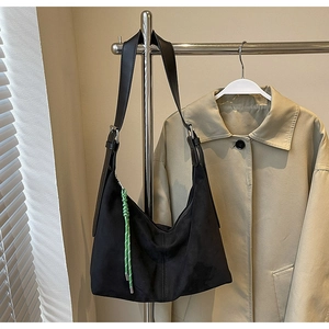 Detail view of black suede hobo tote bag featuring a green braided charm and metal buckle