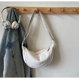 Detail of a white half-moon nylon crossbody bag hanging with headphones and a denim jacket