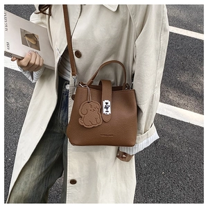 Close-up of brown litchi pattern leather bucket bag with cute dog charm on street view