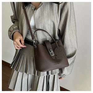 Detail of brown litchi leather bucket bag with lock closure and cute bear charm