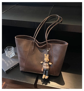 Detail of dark brown matte leather tote bag featuring a cute bunny charm and gold logo