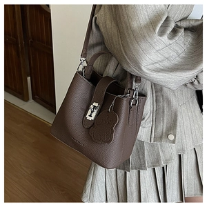 Detail view of dark brown lychee leather bucket bag with silver hardware and bear charm