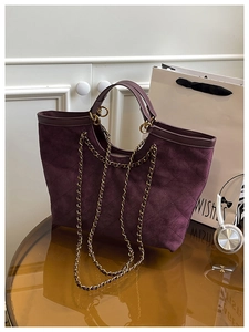 Detailed view of dark purple quilted tote bag with golden chain strap on glass table