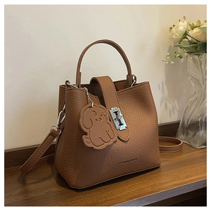 Detail of brown litchi pattern leather bucket bag with metal buckle and puppy charm