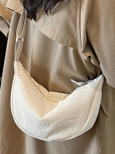 Minimalist beige nylon half-moon crossbody bag shown on model over khaki trench coat