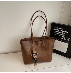 Close-up of brown vintage leather tote with branding and plush bunny charm detail