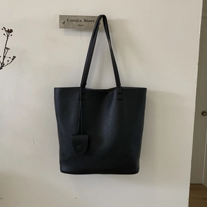 Detail of minimalist black pebbled leather tote bag with slim handles and hanging charm