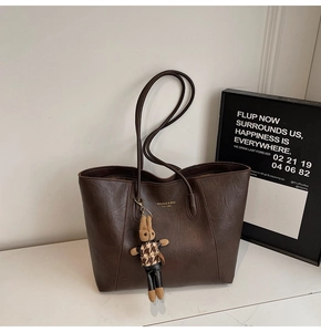 Detail of dark brown tote bag with vintage texture and cute bunny charm on marble surface