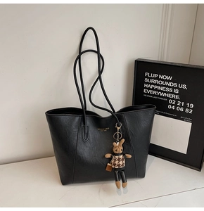 Detail of a black leather tote bag featuring golden logo and cute rabbit charm pendant