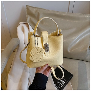 Close-up of yellow pebbled leather bucket bag with metal lock and cute dog charm