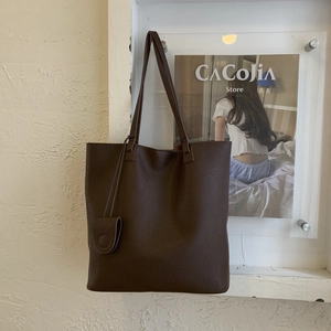 Detailed view of dark brown tote bag featuring pebbled leather texture and matching charm pouch