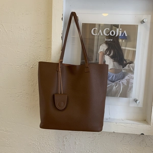 Detailed view of dark brown pebbled leather tote bag with a minimalist charm