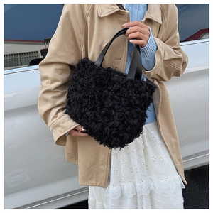Detail of black faux shearling bucket bag with leather handles in outdoor setting