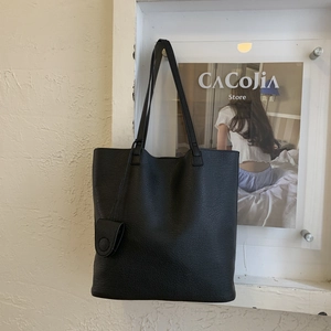 Detail of black pebbled leather tote bag featuring a decorative matching oval pendant charm
