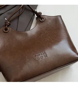 Detail of dark brown leather tote featuring COIH 2DN embossed text and knotted strap