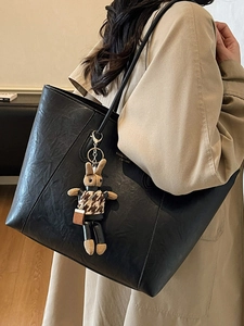 Large black leather tote bag with rabbit charm shown on model in beige trench coat