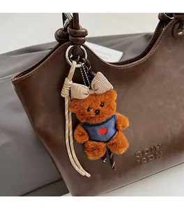 Close-up of a brown plush bear charm with red heart embroidery on blue vest