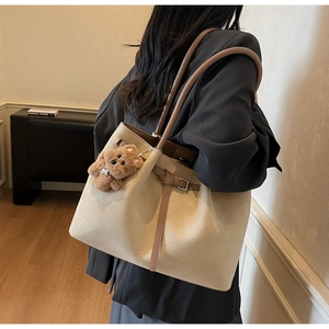 Detail of light beige suede tote bag with brown leather straps and plush bear charm