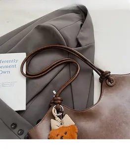 Detail of caramel brown retro tote bag featuring a knotted strap and plush bear charm accent