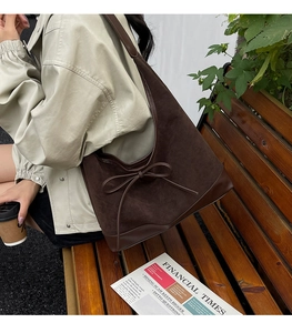 Brown hobo tote bag with leather bow detail styled in a casual city park setting