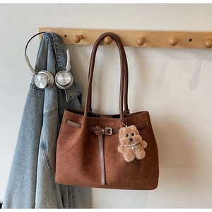 Close-up of brown suede tote bag with belt buckle detail and beige plush bear charm