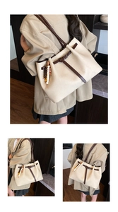 Detail view of large cream tote bag with dark brown leather straps and beaded charm
