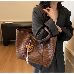 Détail du sac cabas tressé marron avec texture croisée et breloque ours en peluche