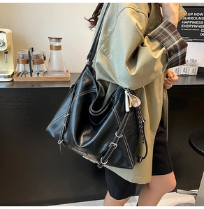 Close-up of black tote bag with white contrast stitching and decorative metal buckles