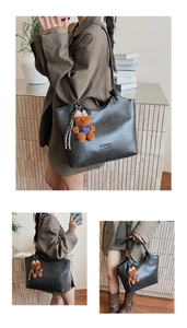 Close-up of black leather tote bag with brand embossing and a cute blue bear charm