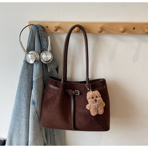 Brown suede tote bag with bear charm and silver buckle detail on a wooden hook