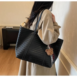 Détail d'un grand sac cabas tressé noir avec fines anses et charm ours en peluche