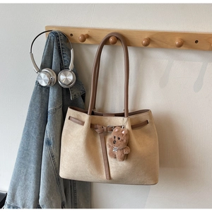 Detail of suede tote bag with brown straps and plush bear charm on a wooden hanger