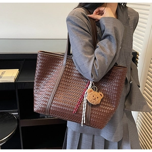Détail du grand sac cabas tressé marron avec breloque ours porté avec un blazer gris