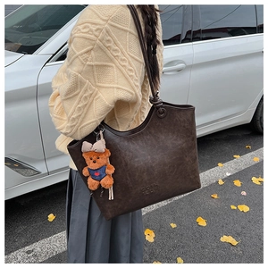 Detail of vintage brown leather tote bag with a blue teddy bear charm in a street setting