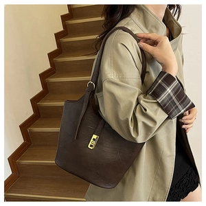Detail of a dark brown vintage leather tote bag worn with a khaki coat on stairs