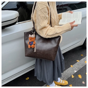 Close-up of vintage brown tote bag with letter embossing and cute bear pendant on strap