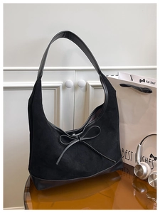 Close-up of black suede tote bag featuring elegant leather bow detail and smooth texture
