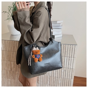 Detail of dark gray tote bag featuring letter embossing and a cute bear plush charm