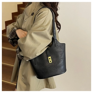 Detail view of black leather tote bag with gold buckle on a model in a studio