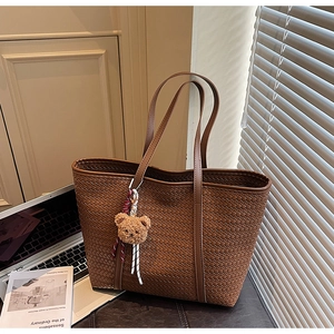 Détail d'un sac cabas tressé marron avec charme d'ours en peluche dans un décor de bureau
